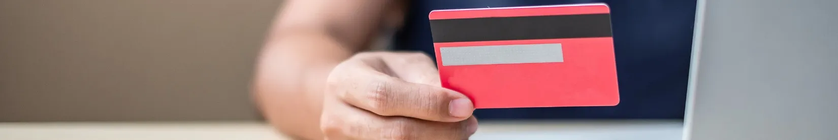 A closeup image of a woman's hand holding a credit card next to a laptop. 